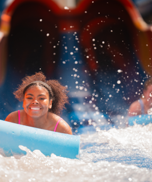 waterpark guest on blue mat splashing in water
