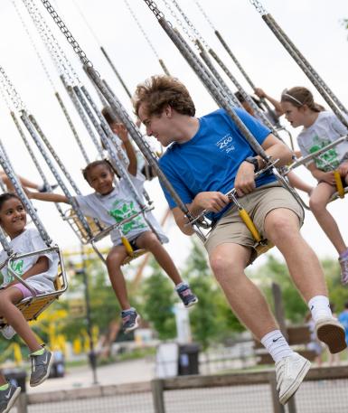 Camp instructor riding on swinging gibbons ride with camp group