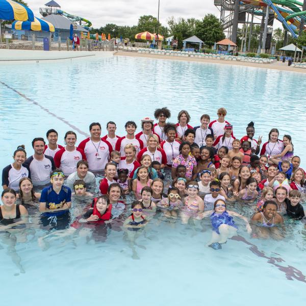 Group of children and lifeguards gather in pool for photo after swim lesson